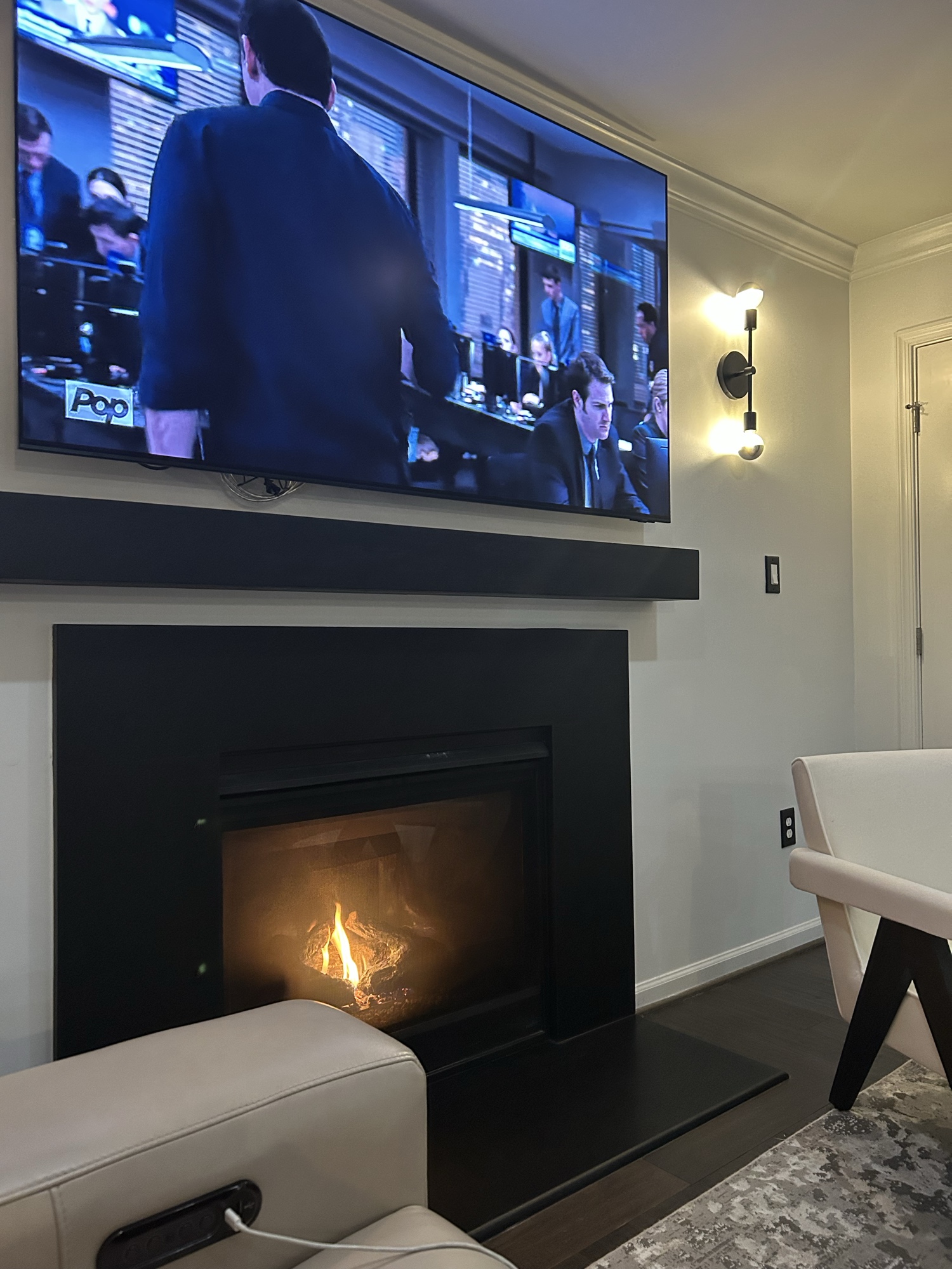 After: dramatic black fireplace surround with floating mantel, mounted television, and twin wall sconces