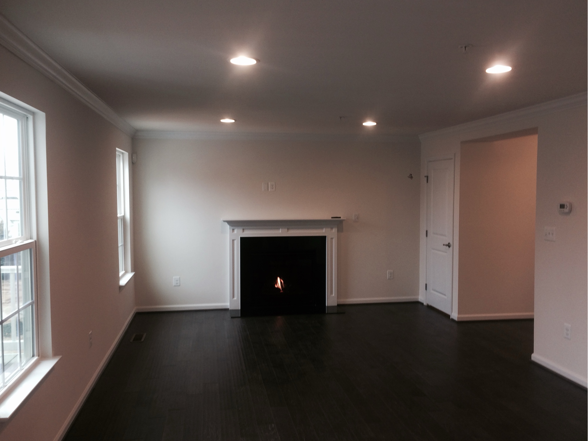 Before: empty living room with dark hardwood floors and a small white fireplace