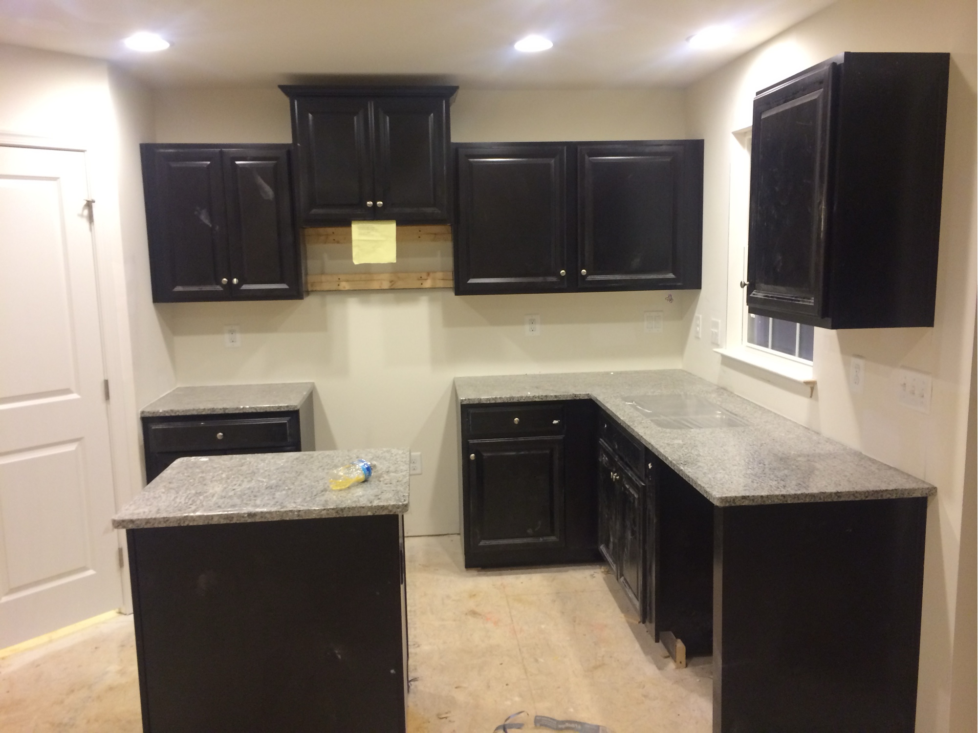 Before: kitchen during construction with dark cabinets, gray granite counters, bare walls, and no backsplash