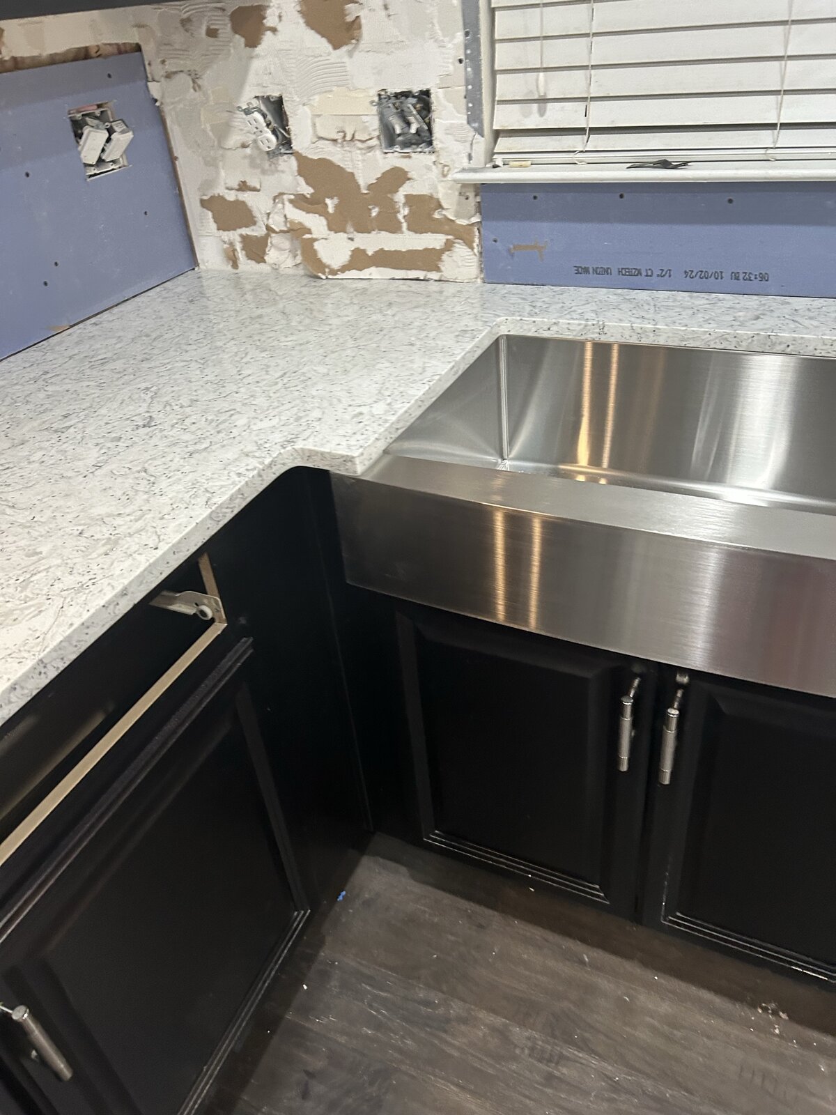During install: corner view of the apron-front sink and quartz counter with the dishwasher in place, before backsplash