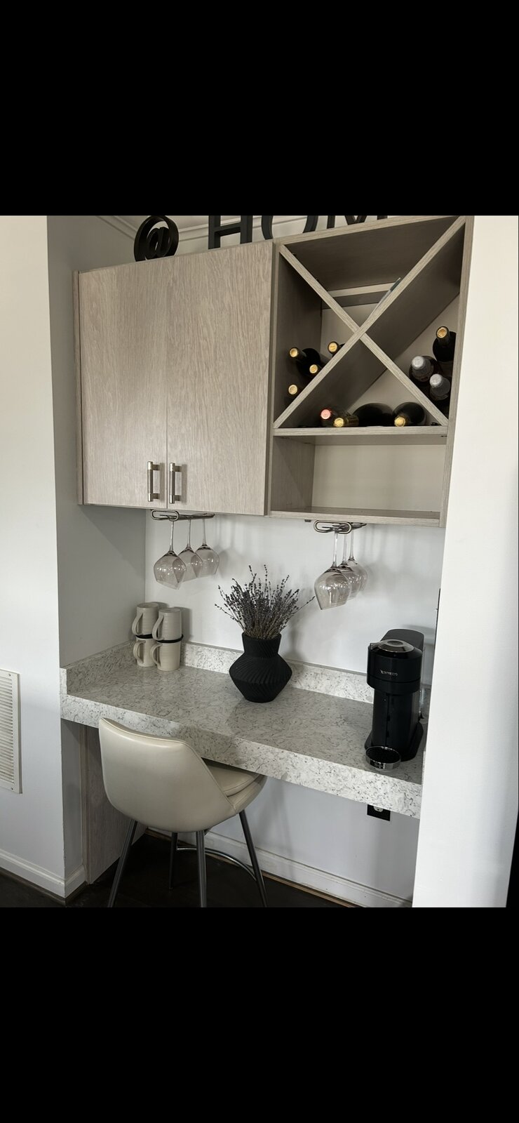 Built-in coffee and wine bar with light oak cabinetry, X-shaped wine rack, hanging stemware, Nespresso machine, and dried lavender in a black vase