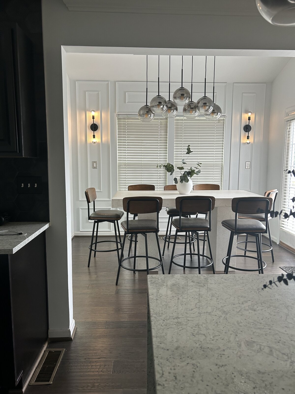 Symmetrical view of the dining room — chandelier centered on the picture-frame moulded wall between twin black sconces