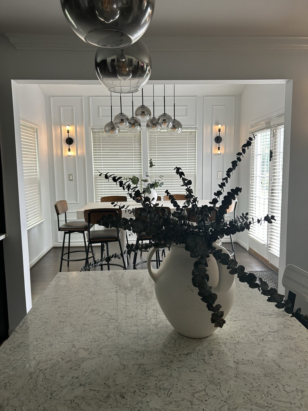 View from the kitchen island through to the dining room, with a white pitcher of dried eucalyptus on the quartz counter in the foreground