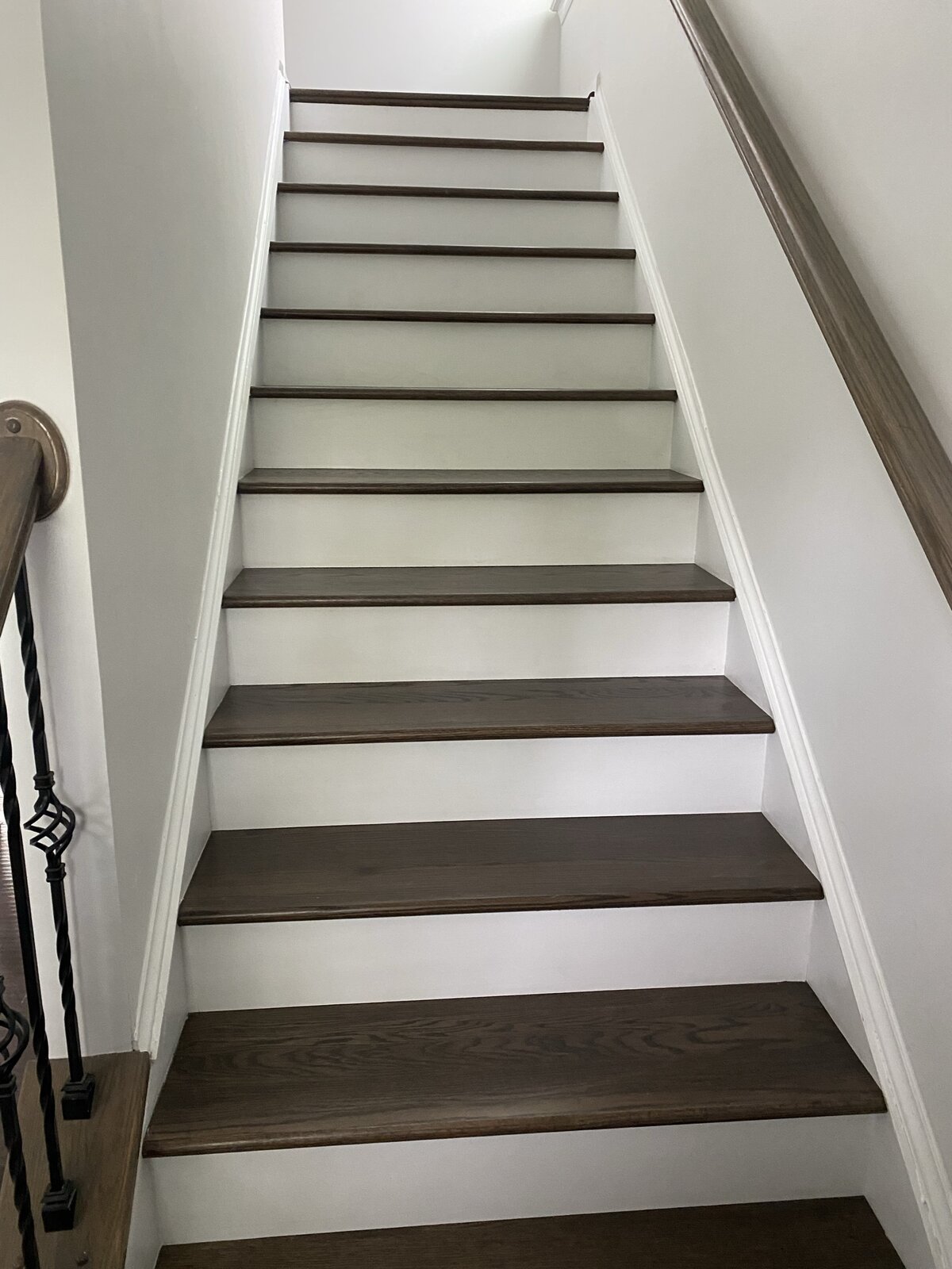 Finished staircase looking down toward landing and front door — same stained oak treads with iron balusters