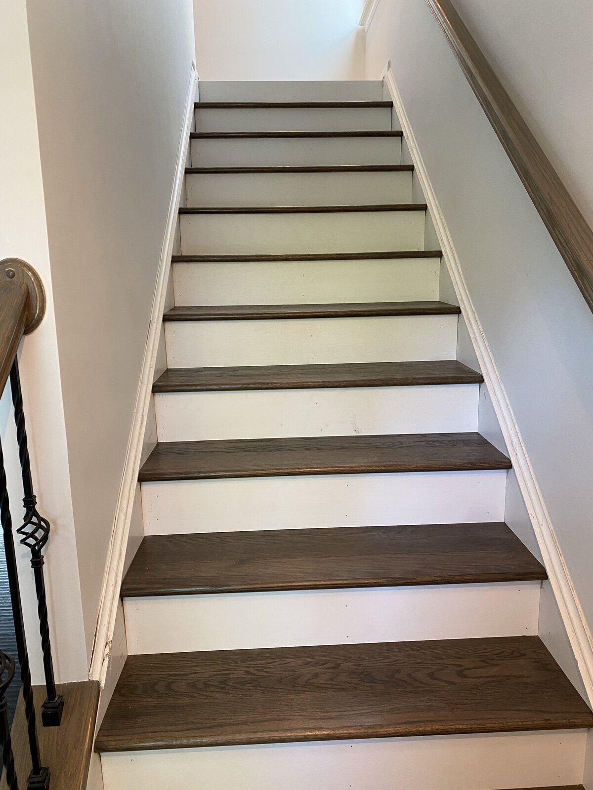 Finished staircase looking up — stained oak treads, white risers, twisted iron balusters, oak handrail