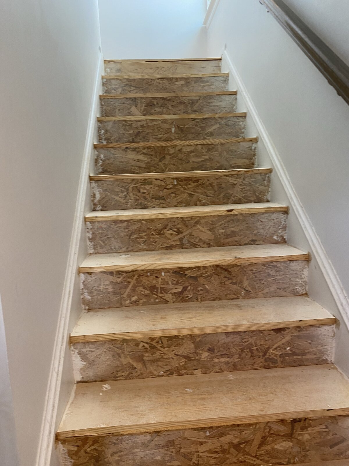 Raw staircase before renovation — OSB subfloor treads, unfinished pine stringers, exposed handrail, looking down toward unfinished basement