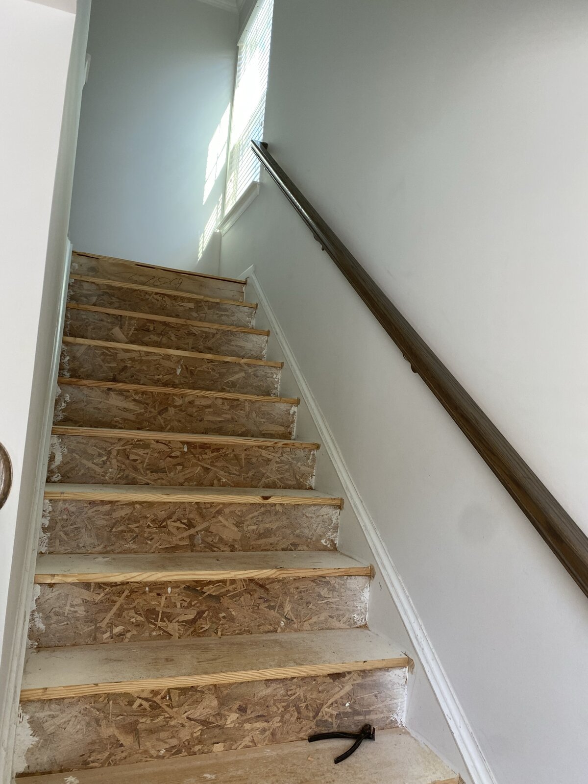 Staircase before renovation — second angle showing the same unfinished OSB treads from the bottom landing